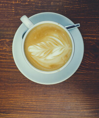 There is a cup of coffee on a wooden brown table during the day