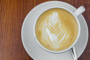 There is a cup of coffee on a wooden brown table during the day