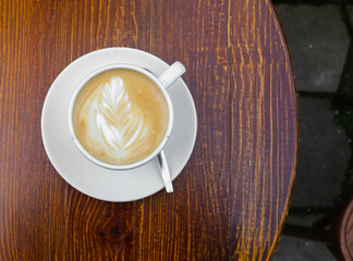 There is a cup of coffee on a wooden brown table during the day