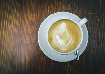 There is a cup of coffee on a wooden brown table during the day