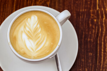 There is a cup of coffee on a wooden brown table during the day