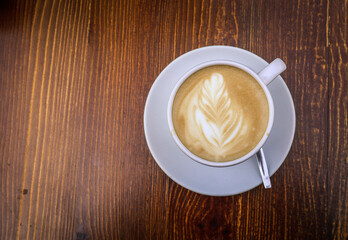 There is a cup of coffee on a wooden brown table during the day