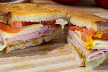 sandwich made of toast, tomato, cheese, ham, lettuce and mustard on wooden surface