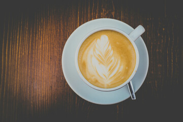 There is a cup of coffee on a wooden brown table during the day