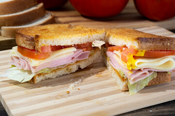 sandwich made of toast, tomato, cheese, ham, lettuce and mustard on wooden surface