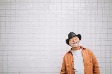 Portrait of happy senior man in hat standing against white wall