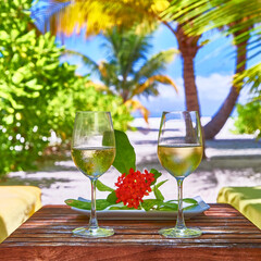 White wine in glasses near deck chair. Maldives beach resort. Amazing view, blue turquoise lagoon water, palm trees and white sandy beach. Luxury travel vacation destination