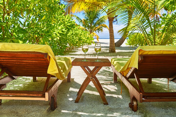 Obraz premium White wine in glasses near deck chair. Maldives beach resort. Amazing view, blue turquoise lagoon water, palm trees and white sandy beach. Luxury travel vacation destination