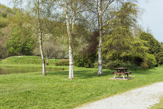 A Beautiful Park All In Green Grass And With Picnic Tables And Rest,