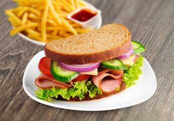 Philly cheesesteak sandwich made with cheese and onions with french fries on a wooden board