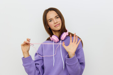 a stunned woman stands on a white background in a purple tracksuit with an uncomprehending look trying to untangle the headphone wire