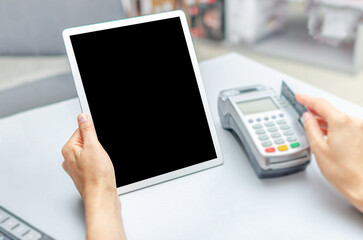 A woman works with a bank terminal and a tablet pc at the table.