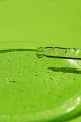 Dropper pipette with serum or cosmetic liquid and petri dish on green background. Transparent...