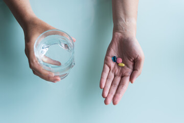 Hand holding omega 3, spirulina, chlorophyll,magnesium capsules above glass of water on wooden table. Morning vitamin pills. Dietary supplements. Health support. Biologically active additives