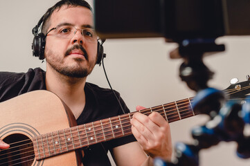 latin caucasian man at home watching guitar lessons on the mobile, perspective from the phone.