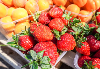 Fresh ripe strawberry and apricots in plastic boxes at the farmer market