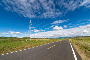 A straight asphalt road under the blue sky and white clouds