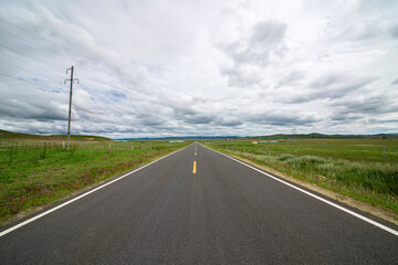 A straight asphalt road under the blue sky and white clouds