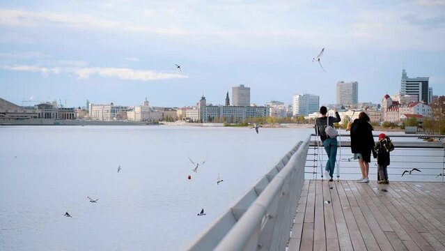 Father, mother and son stand on the bridge and throw bread to seagulls against the backdrop of the city