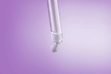 Glass lab dropper with a drop hanging from it on violet background, Abstract cosmetic ingredients...