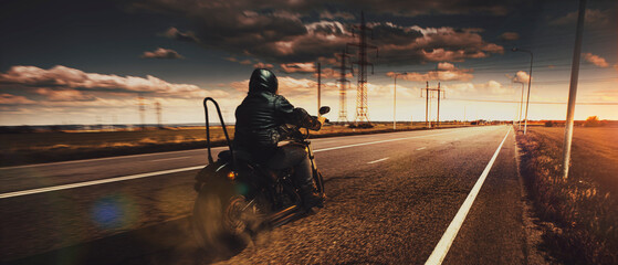 Stylish brutal biker riding motorbike in speed highway in summer evening time. Vintage cinematic background and dramatic cloudy sky. Concept of fashion, style and hobby