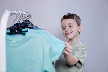 Boy preschooler standing by the hangers, racks up clothes, and chooses clothes for today