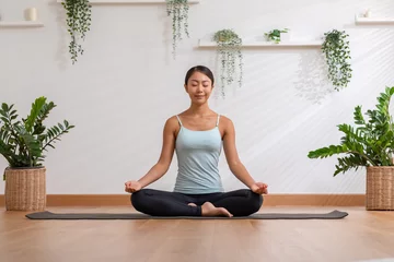  Calm of wellness Asian young woman sit on yoga mat doing breathing with yoga lotus pose.Yoga meditation of young healthy woman relax and comfortable at white cozy home,Yoga Exercise Wellness Concept © 220 Selfmade studio