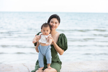 Happy cute baby boy with his mother on the beach. Summertime with baby is a quality time for Asian mommy.  Mother and baby on the beach and happy morning moment. Motherhood love and care for her child