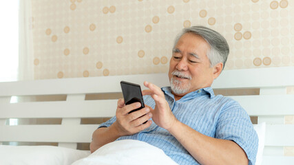 Senior Male using a smartphone , smiling feel happy in bed at home - lifestyle senior concept