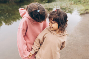 Two stylish casual sisters love and care for each other, children hold hands in nature