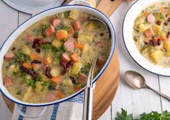 Pot with potato soup, crispy bacon and sausages