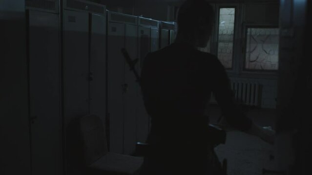 Female apocalypse survivor with shaved head holding flashlight, looting in abandoned dark locker room