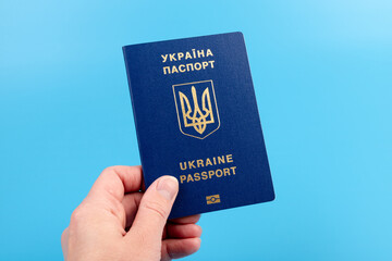 Passport of a citizen of Ukraine in a female hand on a blue background, close-up. Inscription in Ukrainian Ukraine Passport