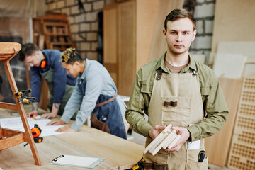 Waist up portrait of young carpenter in coveralls looking at camera while posing in artisan...