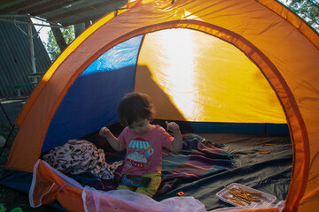 Obraz na płótnie Canvas A child sits in a tent on the lakeshore, watches cartoons on the phone and eats sweets, a girl sits in a tent, tourism, family, summer, vacation, picnic, travel