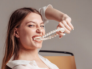 Girl holding pearl beads in her teet. Beautiful smile and white teeth of a young woman. 