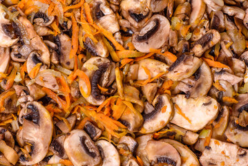 Fried champignons with carrots, onions and spices in a pan against a dark concrete background