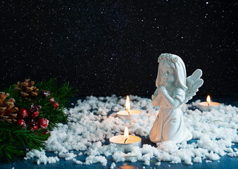 Spruce branches with cones and red berries in the snow. An angel figurine among the candles. Snow...