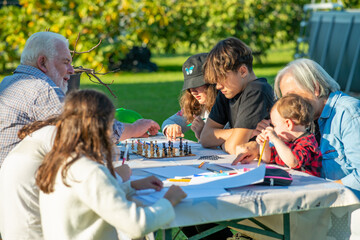 Grandparents and grandchildren playing together outdoor on a sunny afternoon at table games.