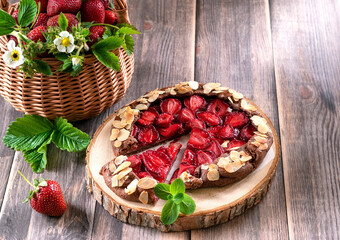 Galette with strawberries. Summer light dessert. French pastry. Open sweet pie with berries. Strawberries in a basket on a wooden background.