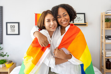 Couple of same sex marriage from difference races holding LGBTQ rainbow flag for pride month to...