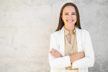 Charismatic smiling positive businesswoman stands with arms crossed over gray wall, confident small...