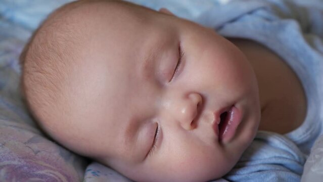 Adorable newborn girl with closed eyes sleeps peacefully in bed. Portrait of little baby with plump cheeks at daytime sleep in nursery extreme closeup