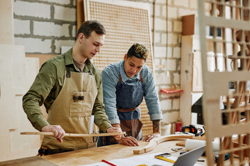 Warm toned portrait of two carpenters designing handcrafted furniture piece in workshop - obrazy, fototapety, plakaty