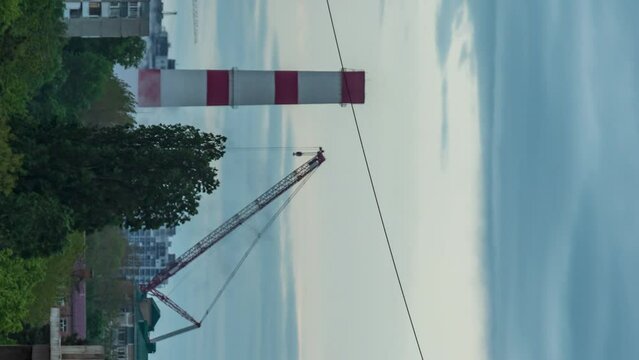 Close-up of the TPP pipe next to the crane against a background of dark rain clouds. Trees ripple in the foreground. The world energy crisis. Smooth departure of the camera. Timelapse. Vertical video