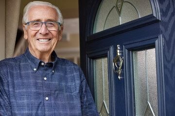 Portrait Of Smiling Senior Man Standing At Open Front Door Of House