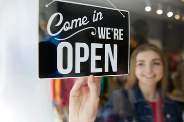 Smiling Female Owner Of Small Business Turning Round Open Sign In Shop Window