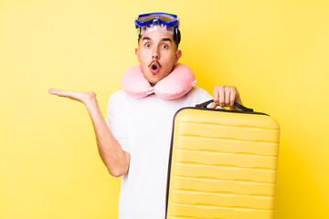 young hispanic man looking surprised and shocked, with jaw dropped holding an object. travel concept
