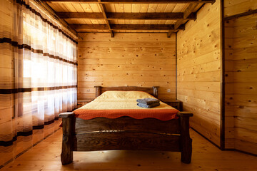 Rustic wooden bed in a cozy cottage room with a double bed, bedside table, blankets and towels. - obrazy, fototapety, plakaty