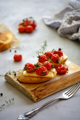 Fried slices of fresh bread with cheese and cherry tomatoes on a wooden board on a gray background. T